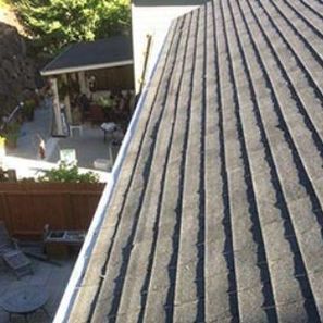 Overhead view of a dark shingled roof with a building and patio visible in the background.