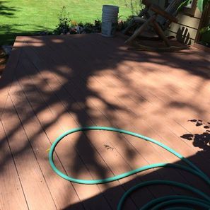 Wooden deck with green hose, shaded by a tree, with grass in background.