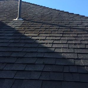 Dark asphalt shingle roof with a chimney and some moss. Blue sky in the background.