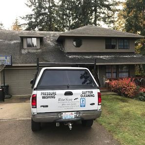 White pickup truck with business signage parked in front of a two-story house, advertising pressure washing and gutter cleaning services.