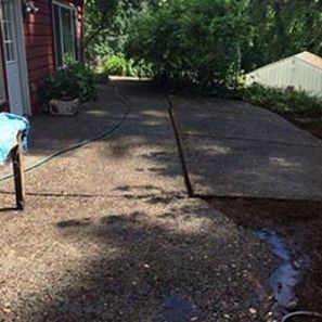 Concrete patio beside a red house; hose, potted plants, and water runoff present.