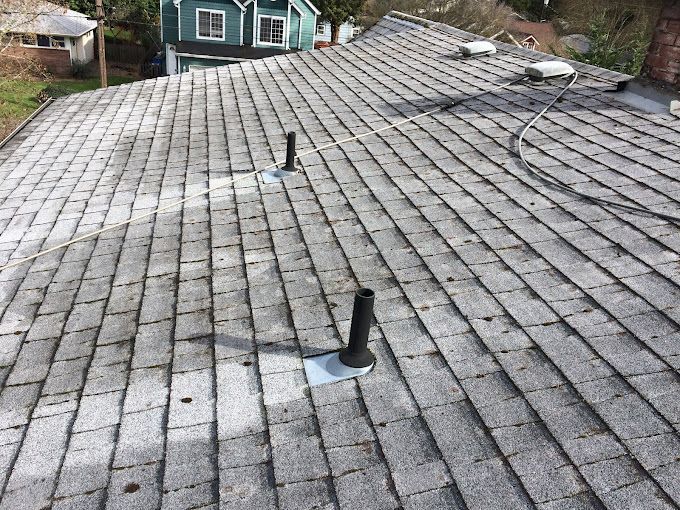 Gray asphalt shingle roof with two black pipes and a view of a neighborhood.