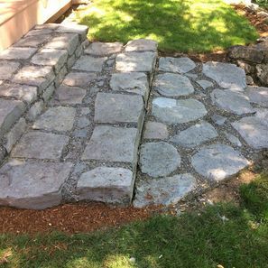 Stone steps leading up, transitioning to a patio of irregular stones, all set in a grassy yard.