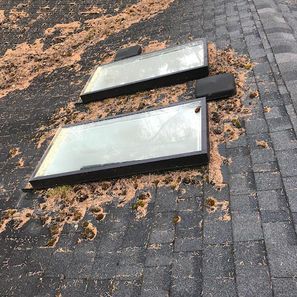 Two rectangular skylights on a dark shingled roof, covered with debris.