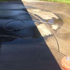 Concrete driveway, half cleaned with a pressure washer, showing stark contrast between dirty and clean areas.