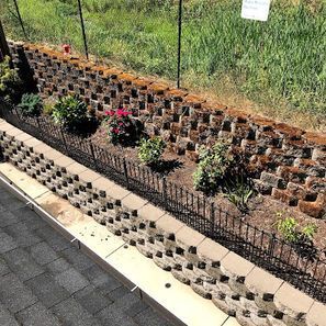 Retaining wall made of modular blocks, planted with flowers and shrubs, next to a grassy area.