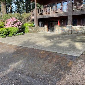 Concrete driveway in front of a multi-story wood building with a porch. Pink flowering bush in the background.