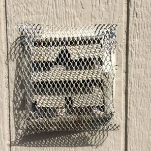 Metal mesh over a vent on a light-colored building exterior.