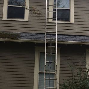 Ladder leaning against a two-story building with siding and windows.