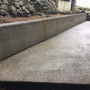 Gray concrete patio with a retaining wall next to a rock garden.