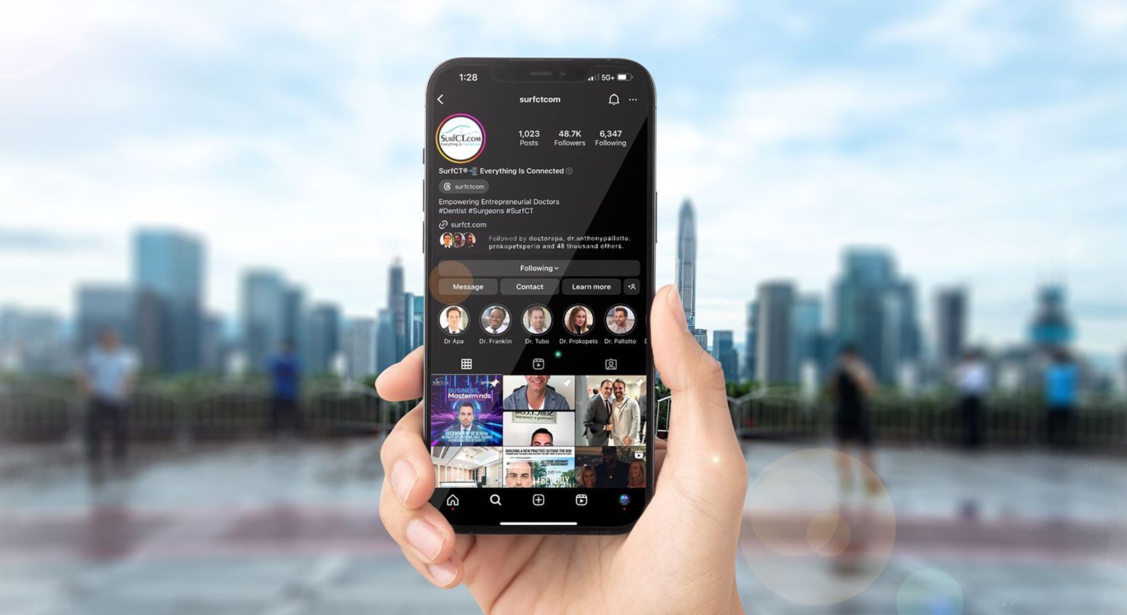 A hand holding a phone displaying a social media profile with a cityscape background.