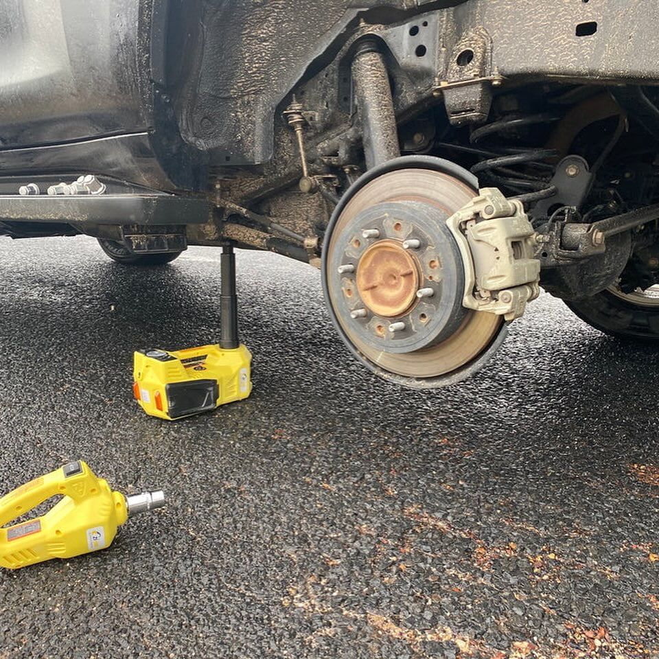 A Car's Rear Wheel is Removed, Jacked Up With Yellow Tools — Alice Springs Auto Parts in Ciccone, NT