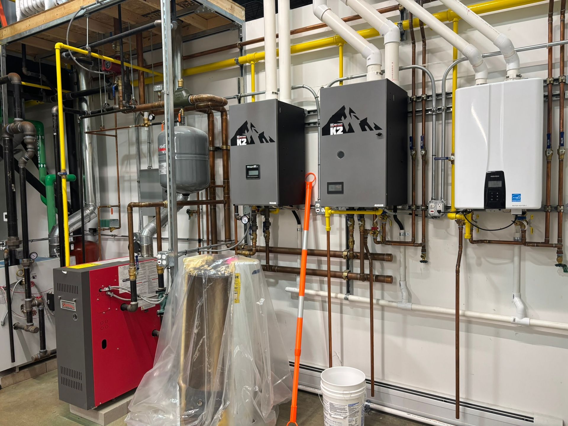 Plumbing installation: multiple water heaters and pipes against a wall, mostly in neutral colors.