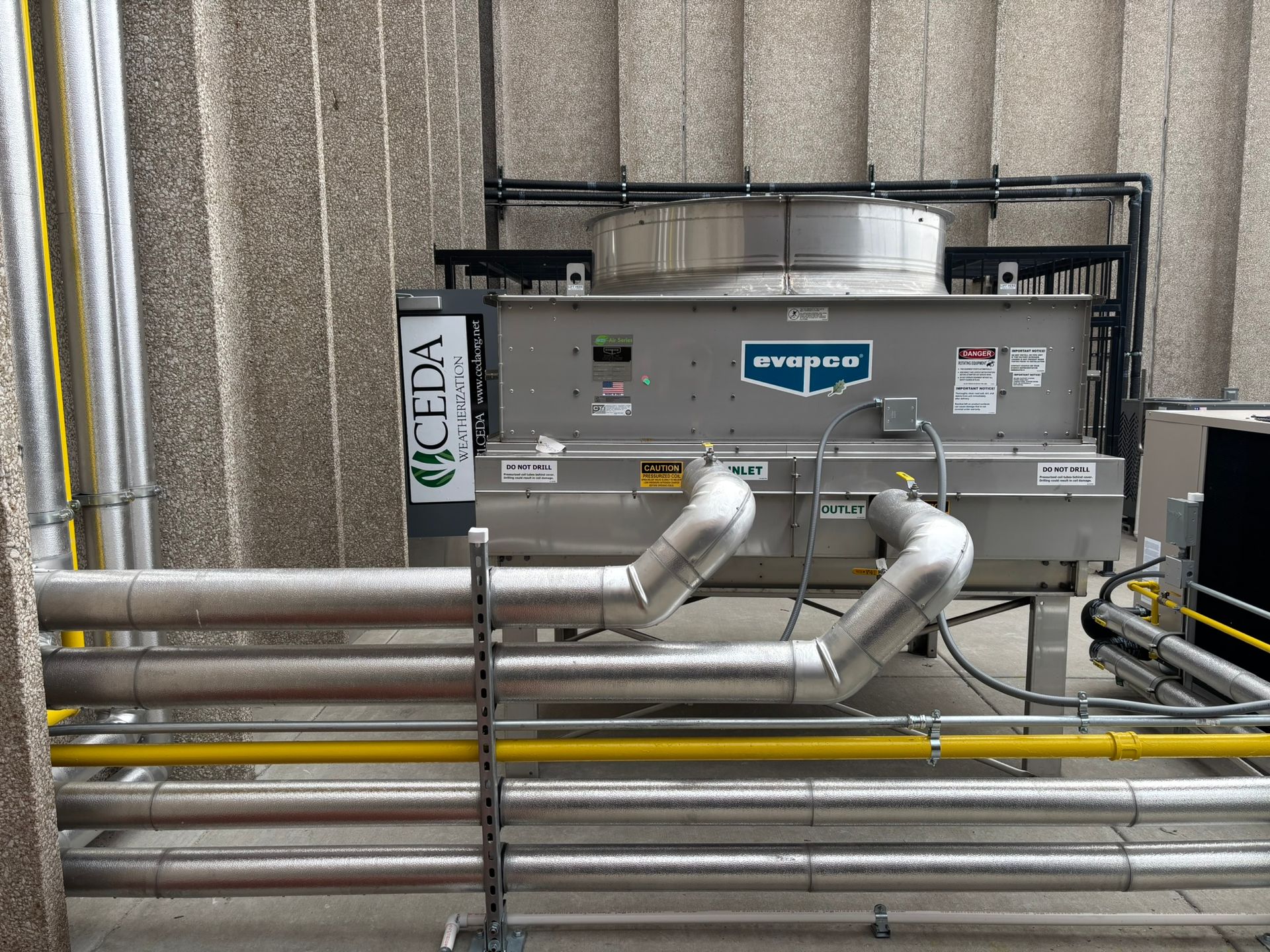 Industrial air conditioning unit on a building rooftop with pipes and vents.