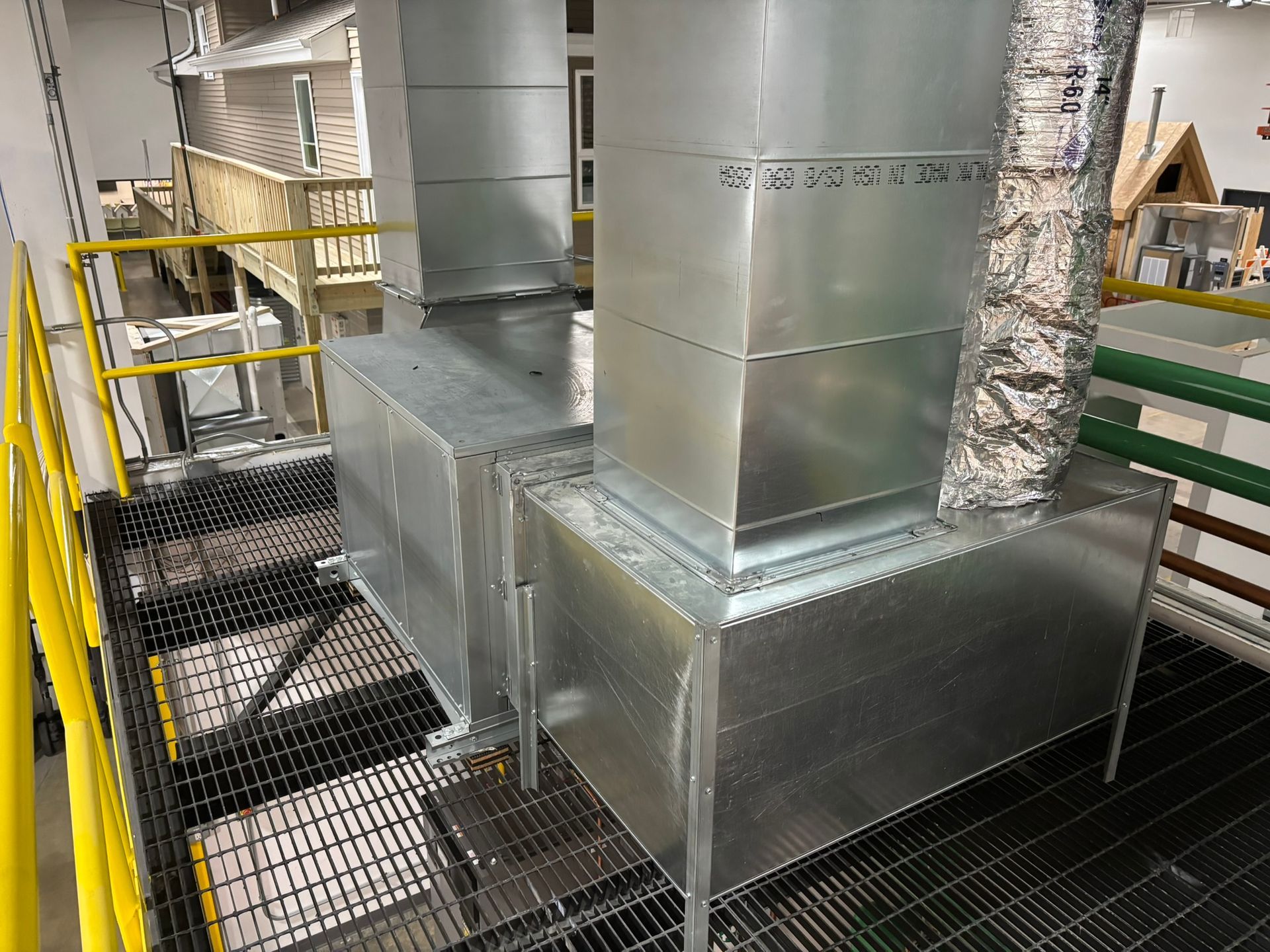 Galvanized metal ventilation system on a metal grated platform with yellow railing.