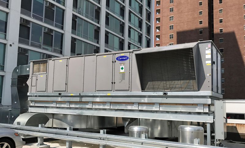 Large, gray rooftop HVAC unit on a building with metal ductwork, and the Carrier logo.