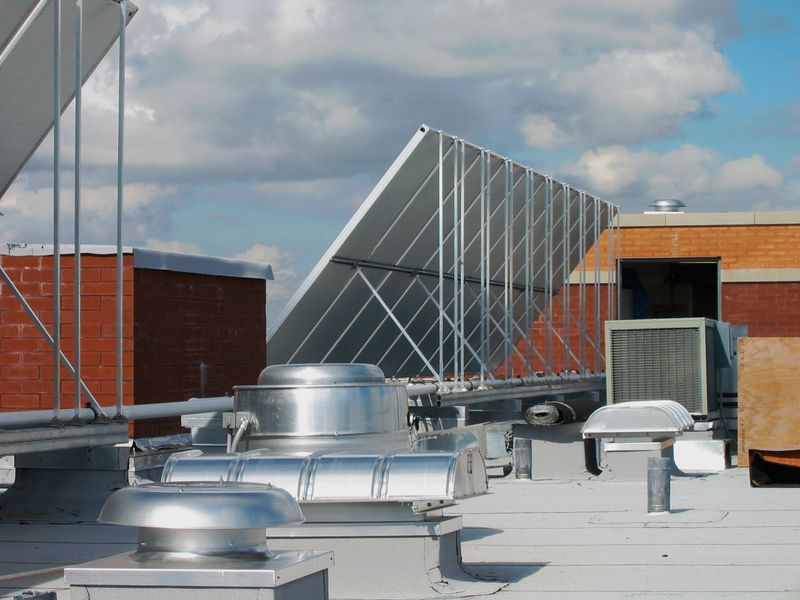 Rooftop with HVAC equipment, brick chimneys, and a large, angled solar panel array under a cloudy sky.