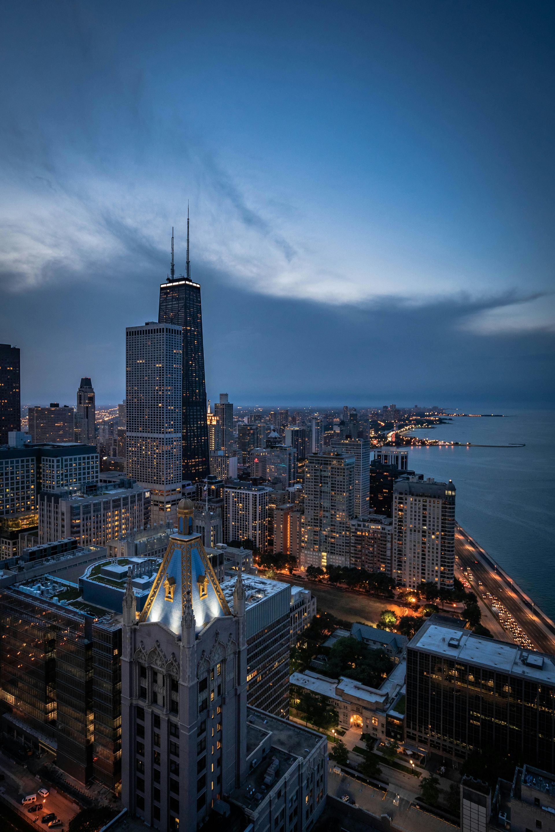 Chicago skyline at dusk with lit buildings, lake and cloudy sky.