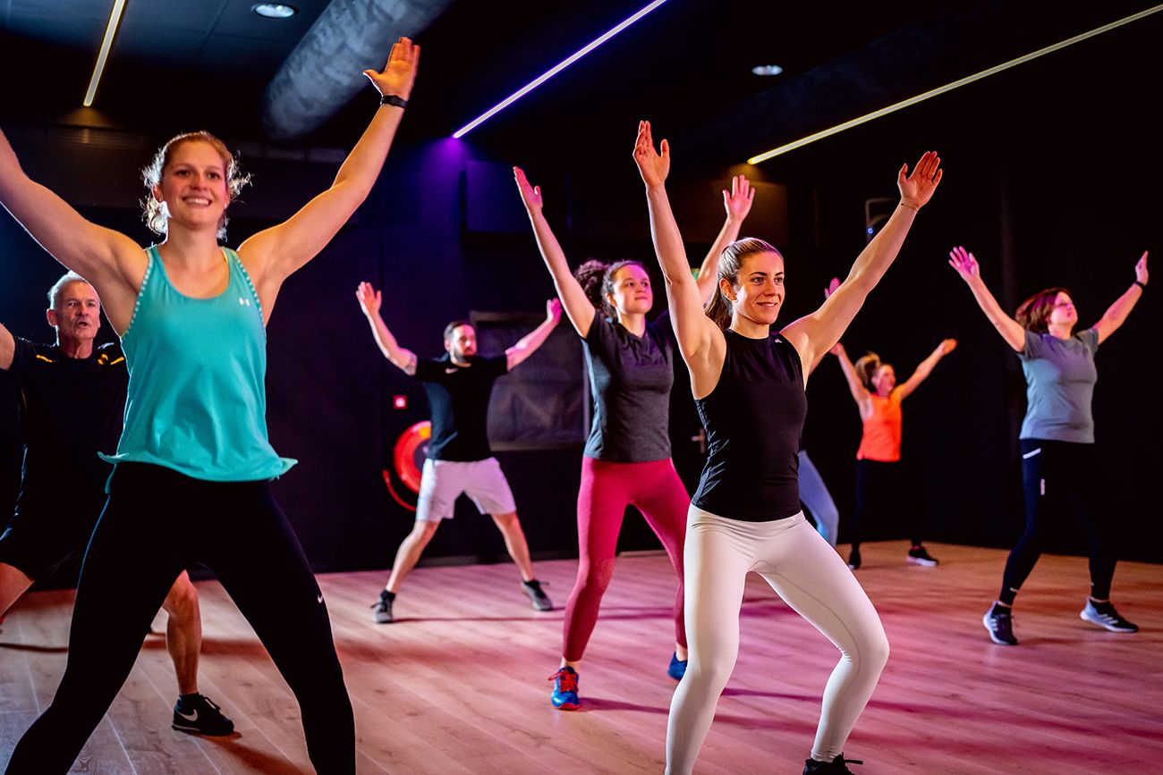 Een groep mensen danst in een sportschool met hun armen in de lucht.