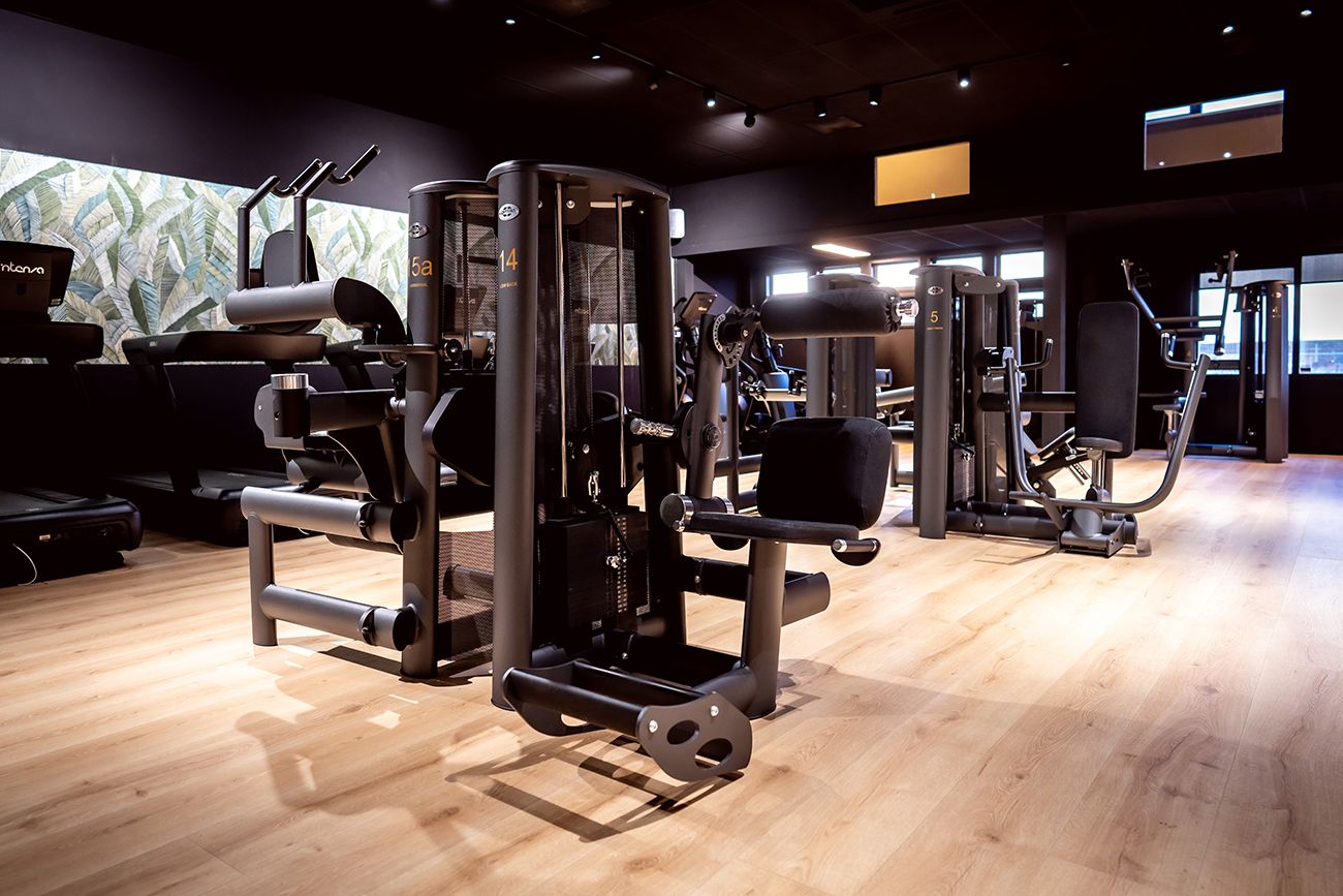 Interieur van een sportschool met verschillende fitnessapparaten op een houten vloer.