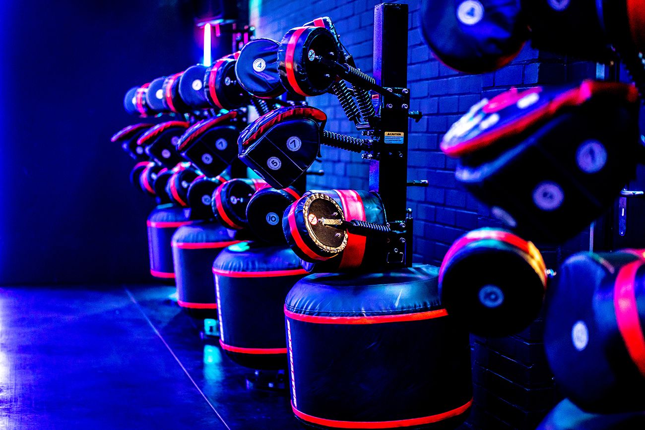 Een rij zwarte boksstations met rode accenten in een gymzaal, verlicht met blauw licht.