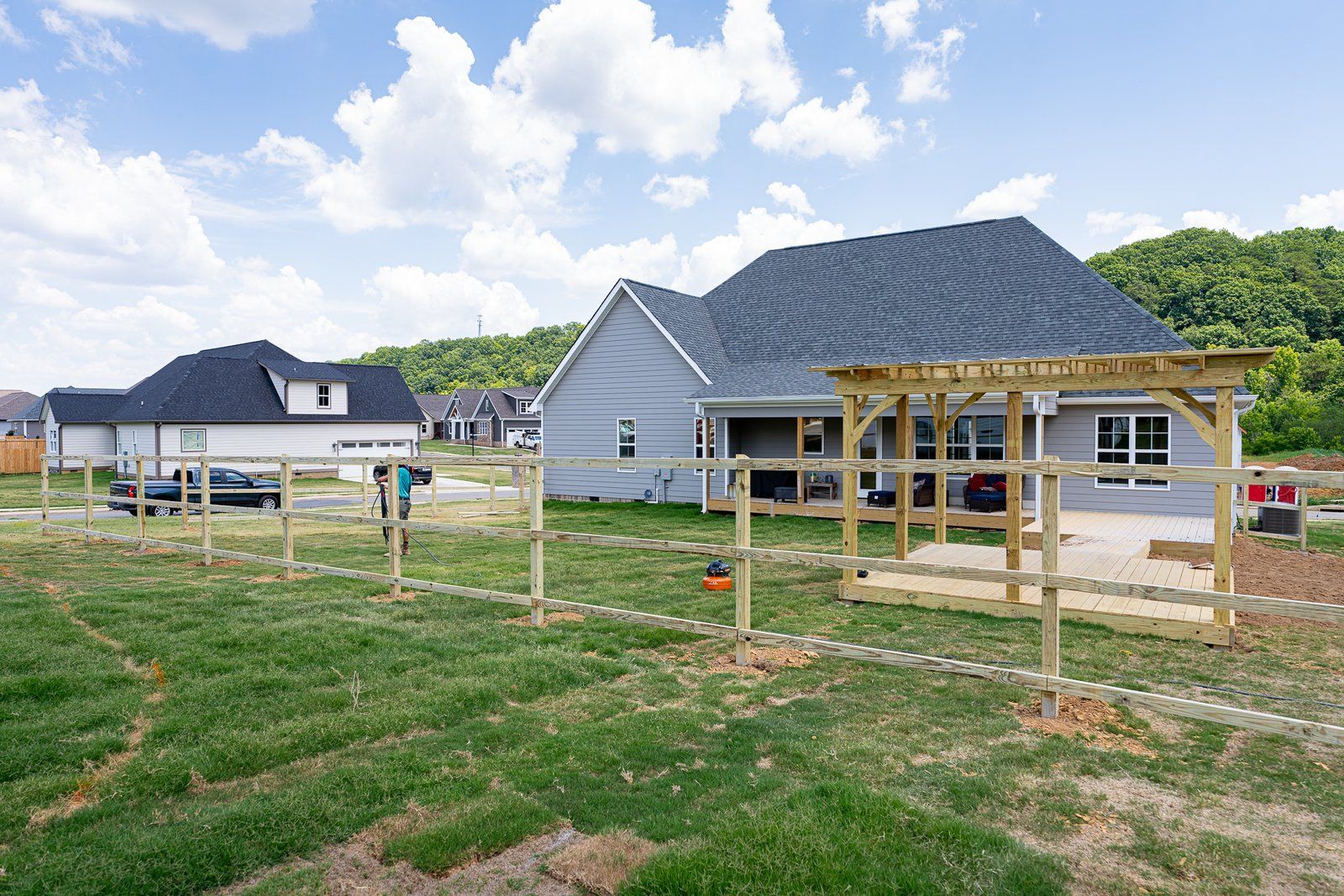 Houses with newly built wooden pergola and fence in a grassy yard under a cloudy sky.