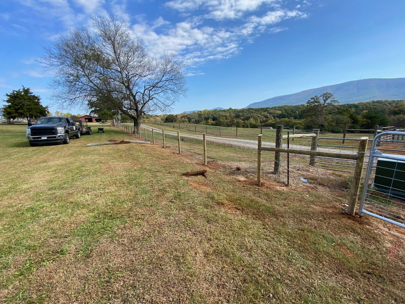 Fence being built in a grassy field with a tree and mountains in the background. Trucks parked nearby.