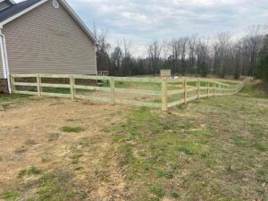 Wooden fence around a grassy yard, beside a house with a cloudy sky in the background.