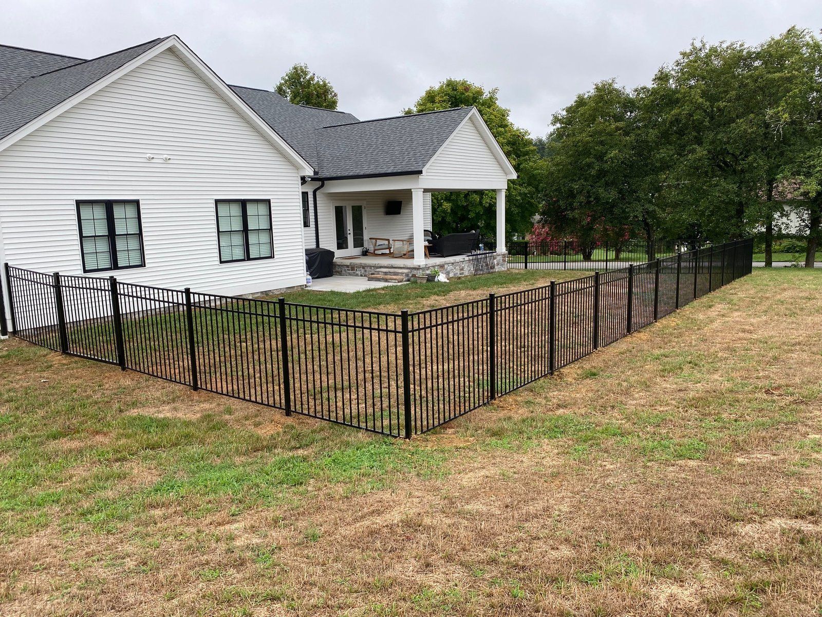 Black metal fence surrounding a white house with a covered porch, set on a grassy lawn.