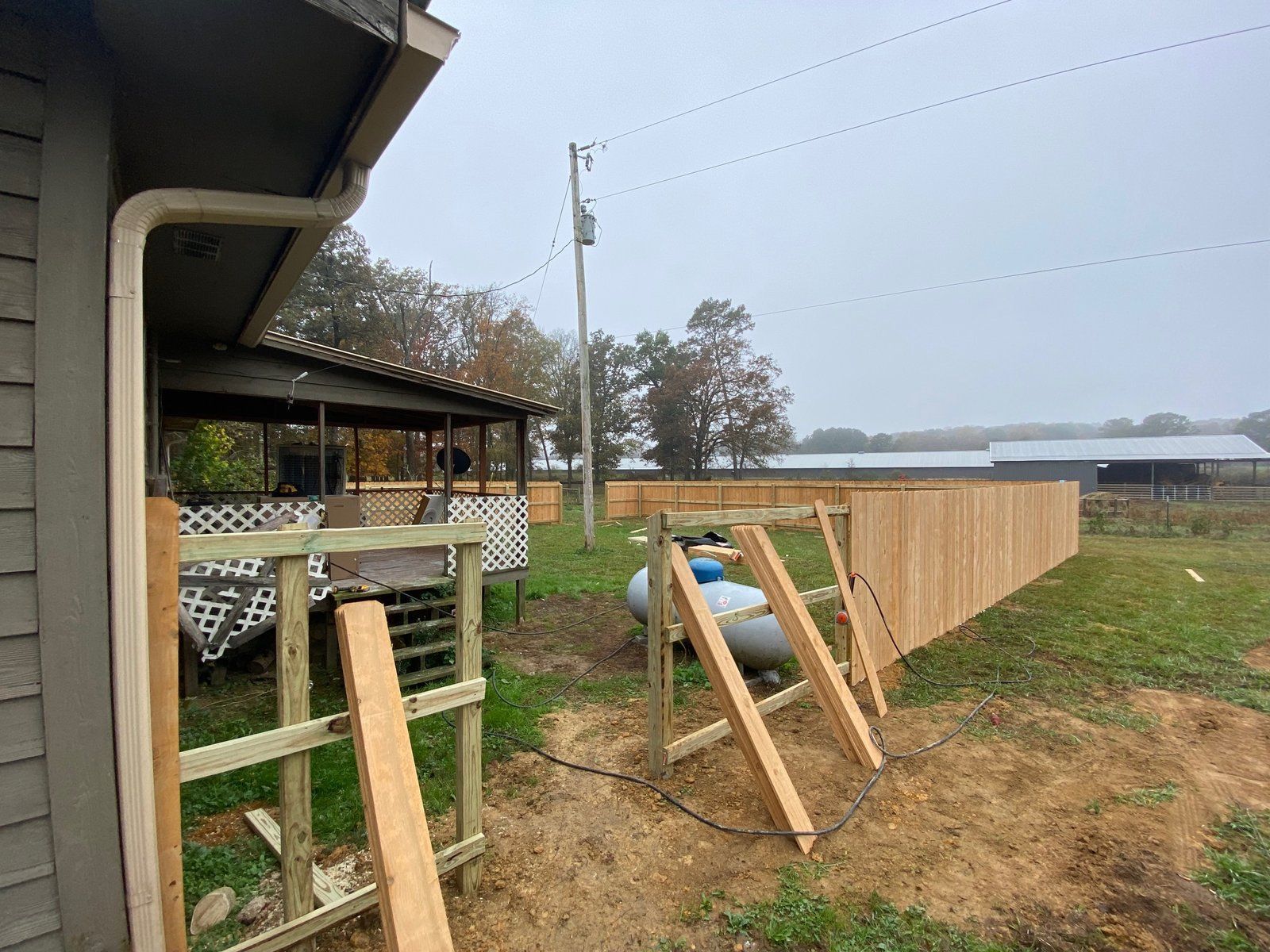Exterior view of a house with a wooden fence being constructed. Gray siding, green grass, and a cloudy sky.