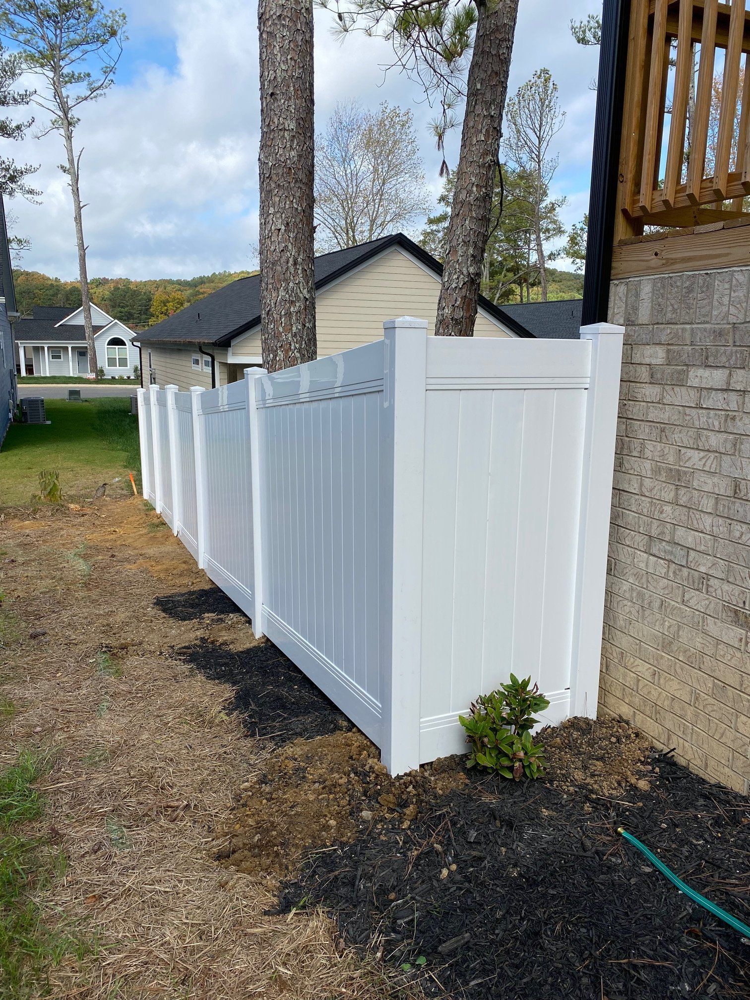 White vinyl fence next to a brick wall and trees. Backyard setting.
