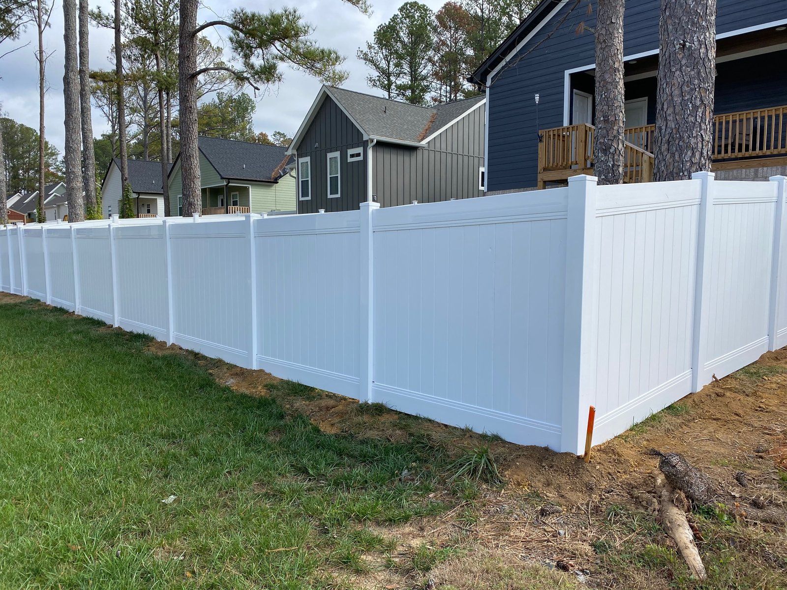 White vinyl fence along green grass, with houses in the background.