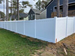White vinyl fence in front of green grass, houses in the background.