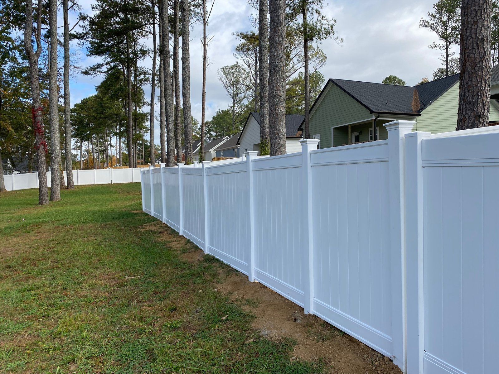 White vinyl fence in a yard, trees in the background, houses beyond.