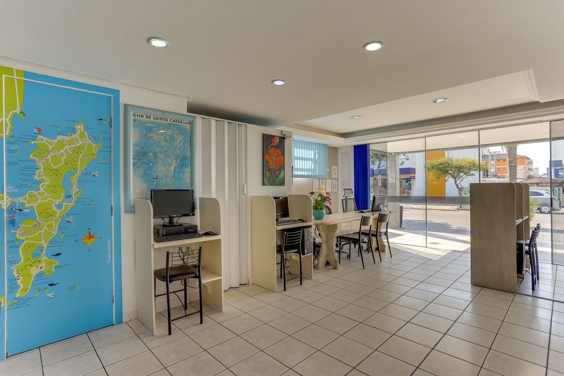 Interior de um escritório bem iluminado com mesas, cadeiras, mapas e grandes janelas.