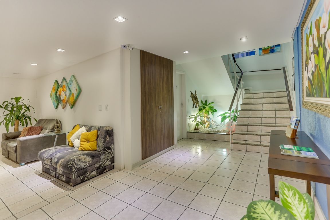 Interior com escada, sofás, vasos de plantas e armário com painéis de madeira.