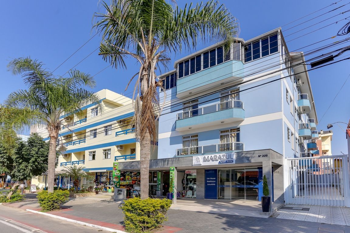Edifício de hotel com fachada azul e amarela, palmeiras e calçada em um dia ensolarado.