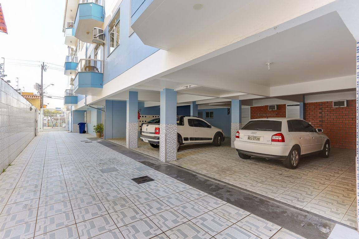 Estacionamento sob um prédio azul claro com carros brancos estacionados dentro.