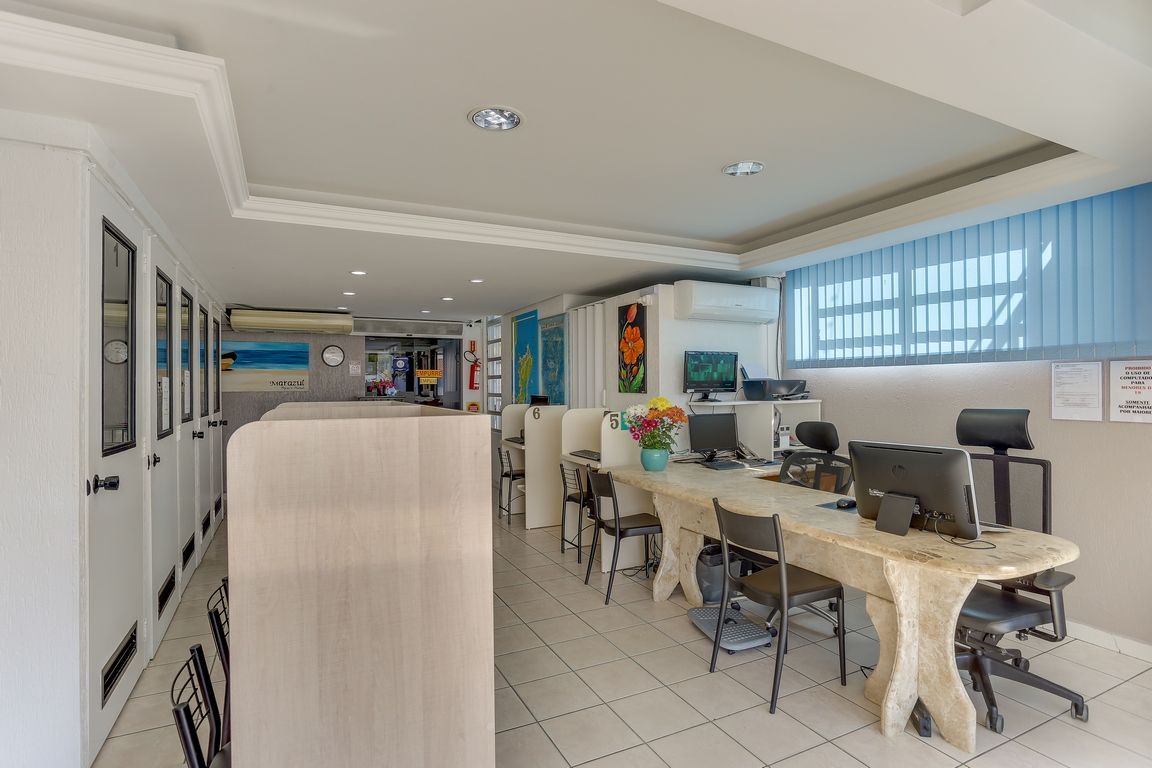 Escritório com computadores, mesa longa, cadeiras e paredes brancas.