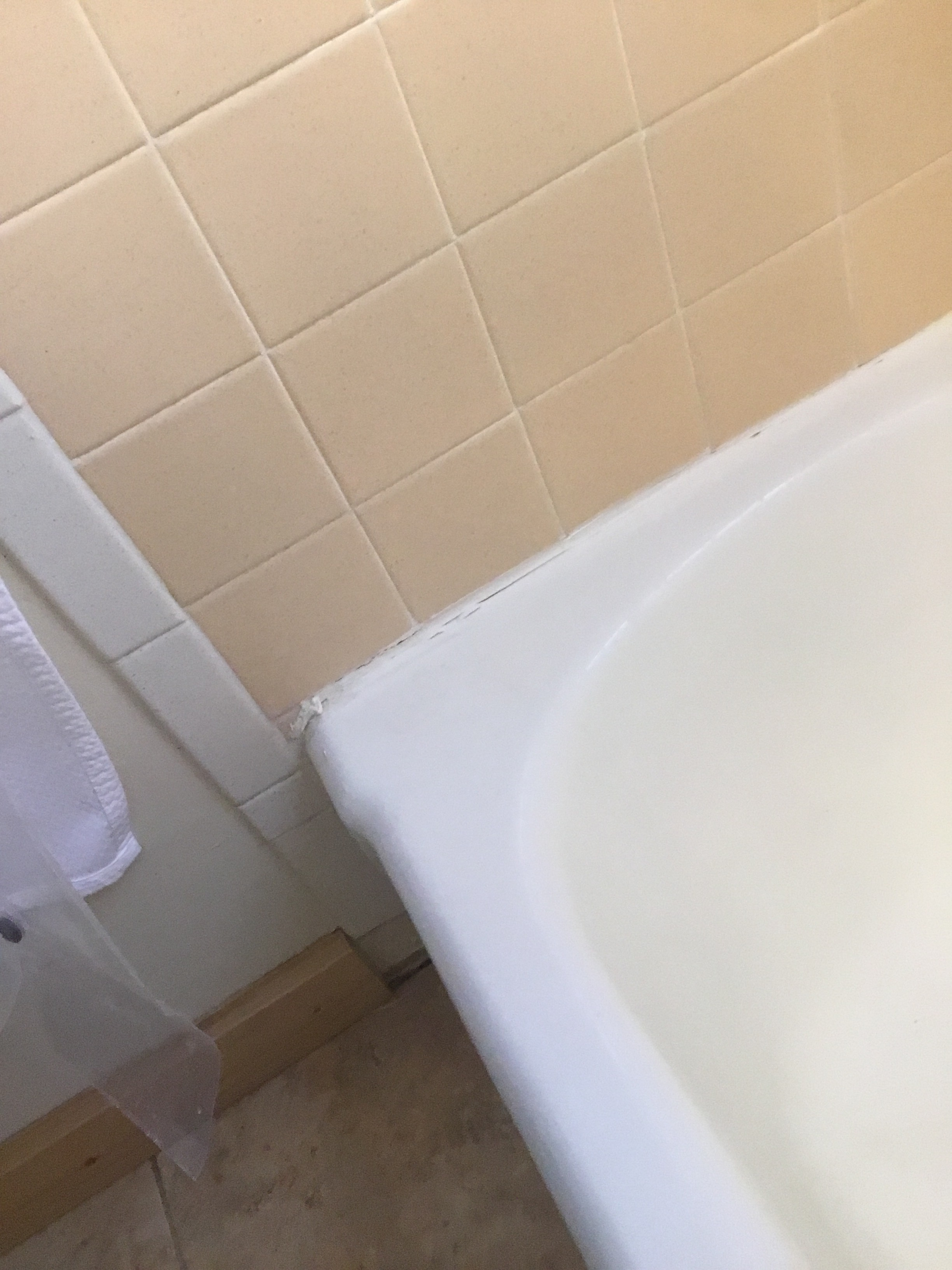 Corner of a bathroom with beige tiles and a white bathtub.