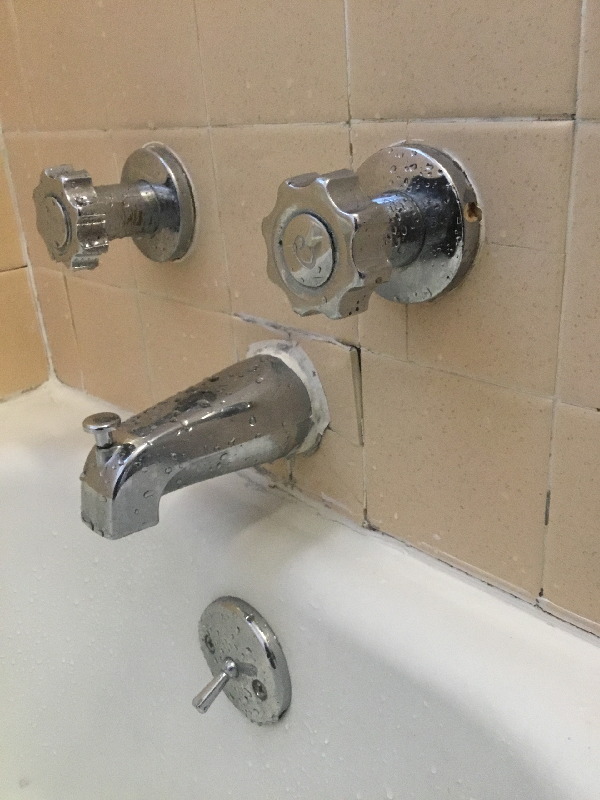 Chrome bathtub faucet with knobs on tan tile.