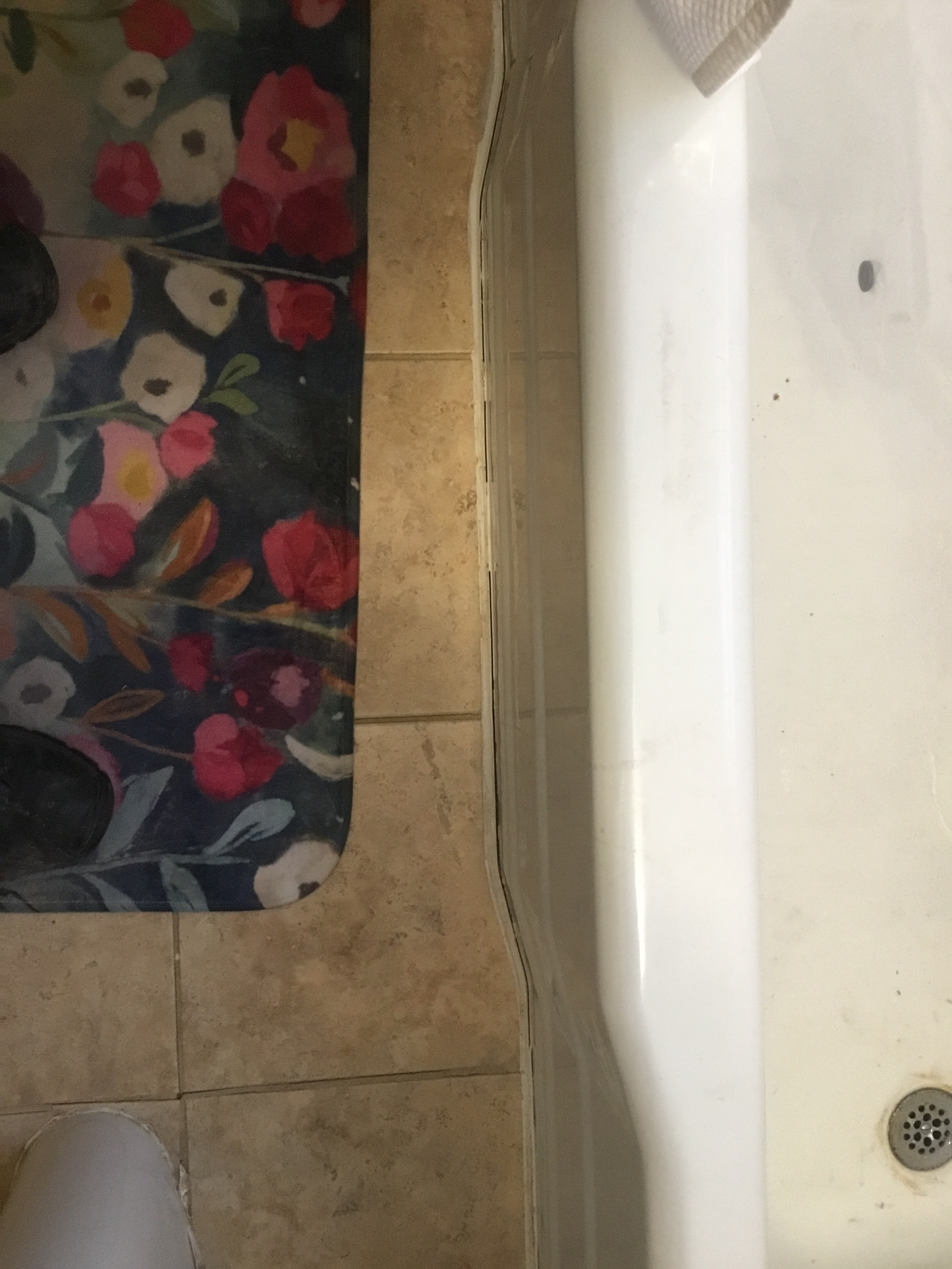 Bathroom with floral bath mat, beige tile, and white bathtub.