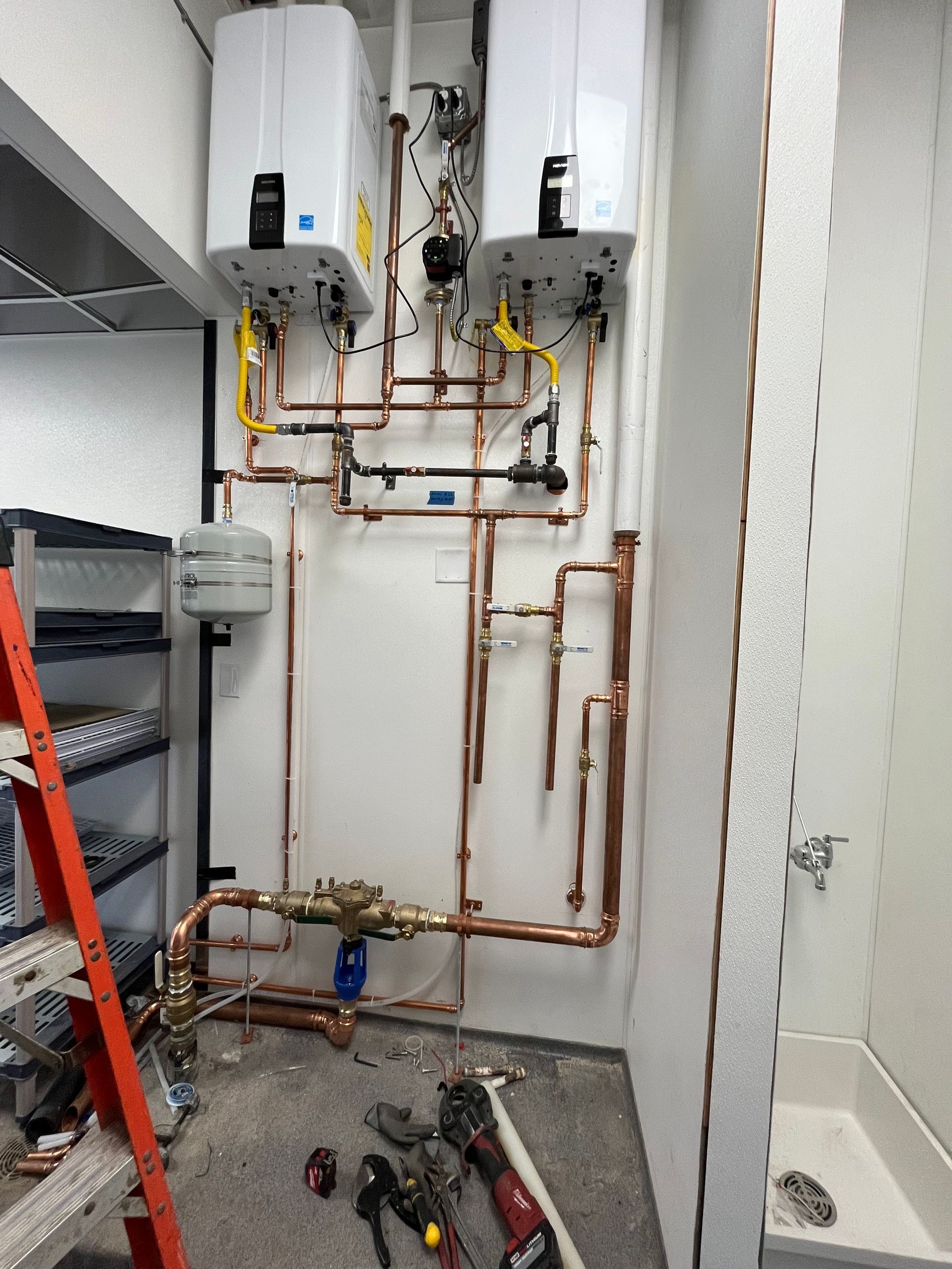 Copper pipes and water heaters installed on a white wall in a utility room.