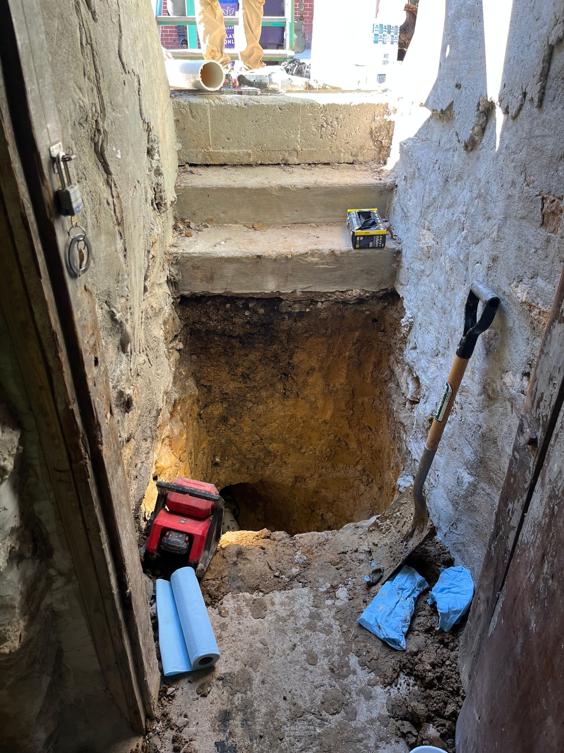 Concrete steps leading up, excavation pit, shovel, tools, pipes, and a door frame.