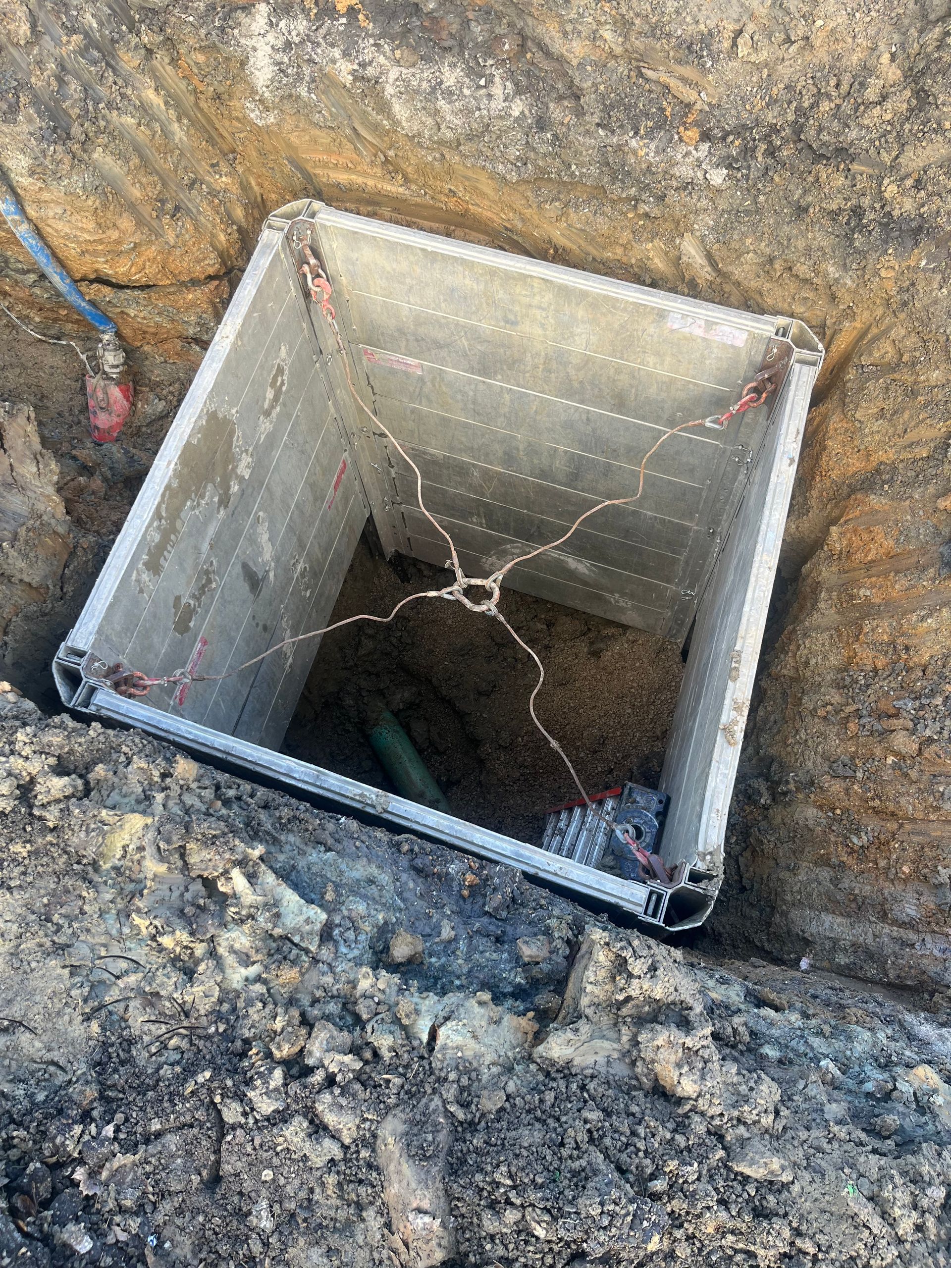 Square concrete utility box in an excavated hole, with wires visible inside.