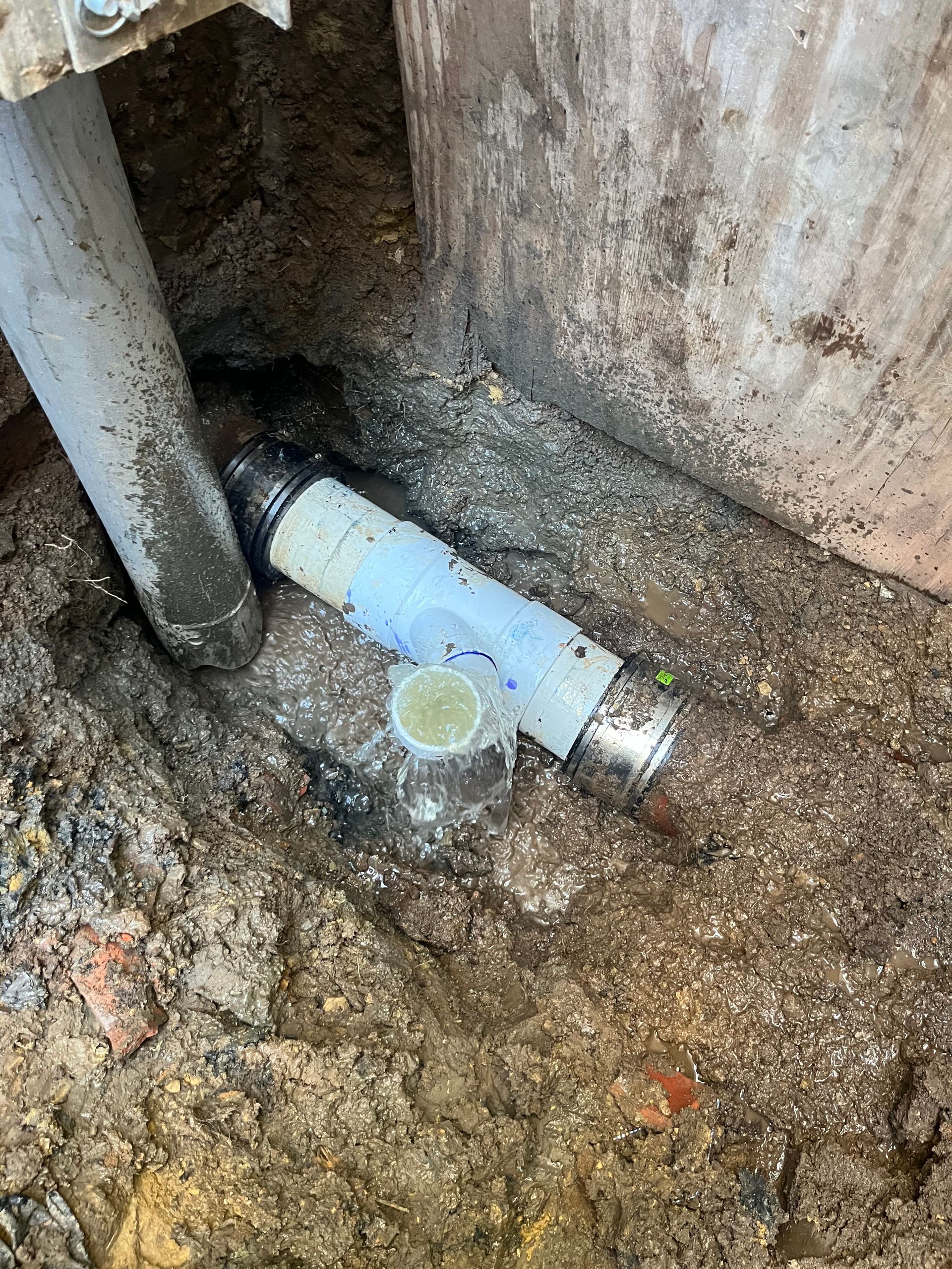 White pipe segment with silver couplings buried in dirt, next to a concrete structure.