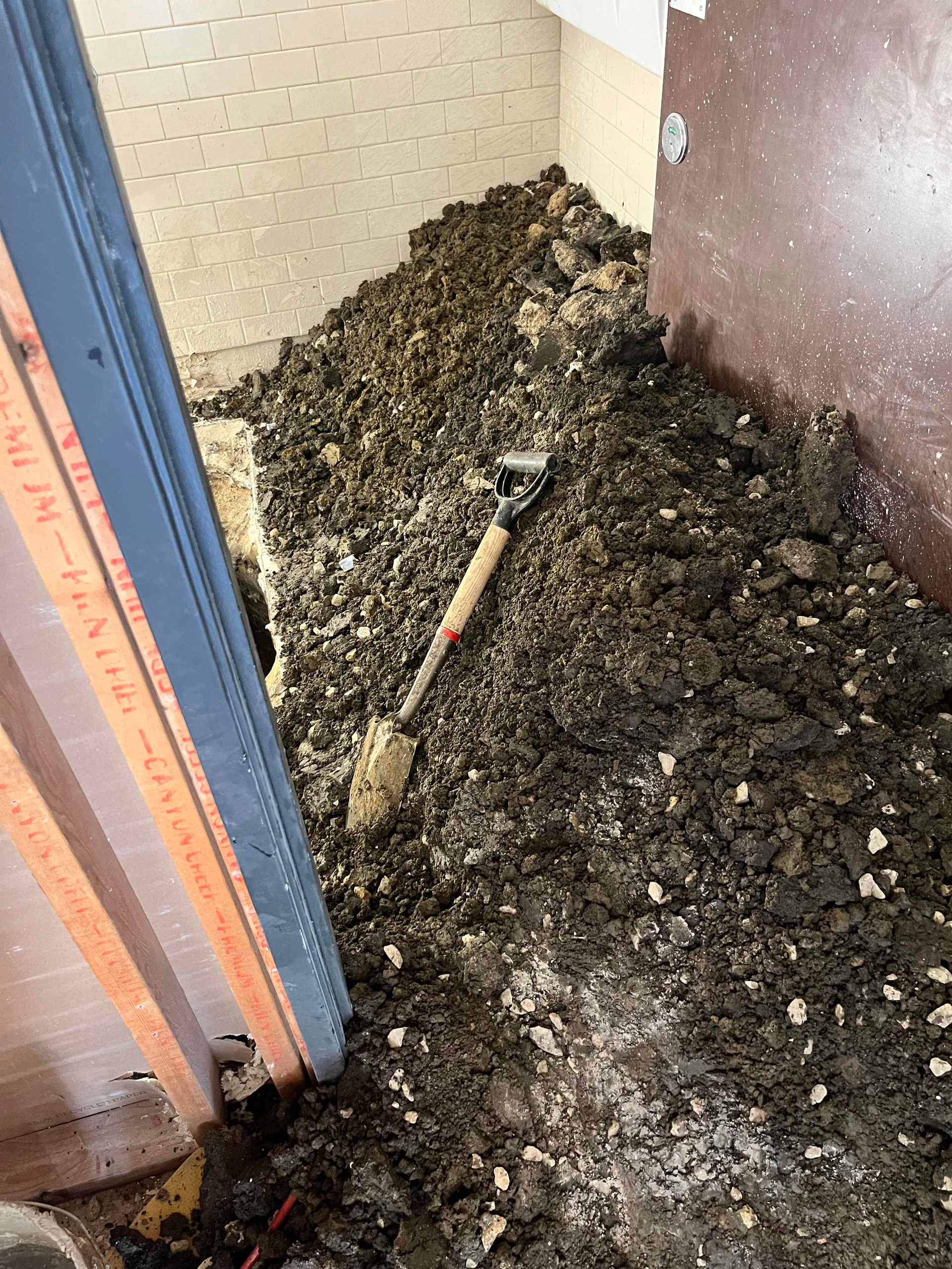 Pile of dirt and a shovel inside a doorway; brown wall and trim on both sides.