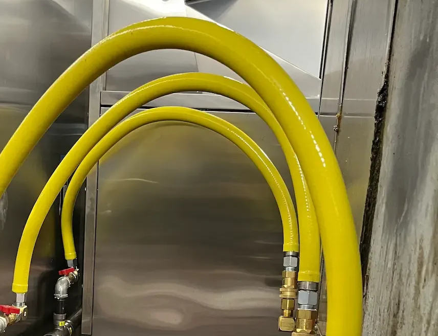 Yellow hoses connected to metal fixtures against a stainless steel background.