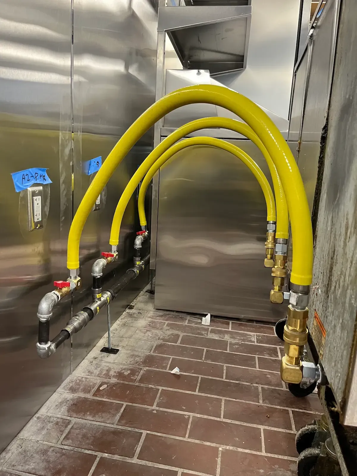 Yellow gas supply hoses arching over a stainless steel kitchen appliance, installed in a commercial space.