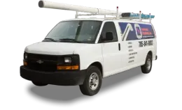 A white plumber's utility van with a pipe carrier on the roof, seen from a front-side angle against a plain background.